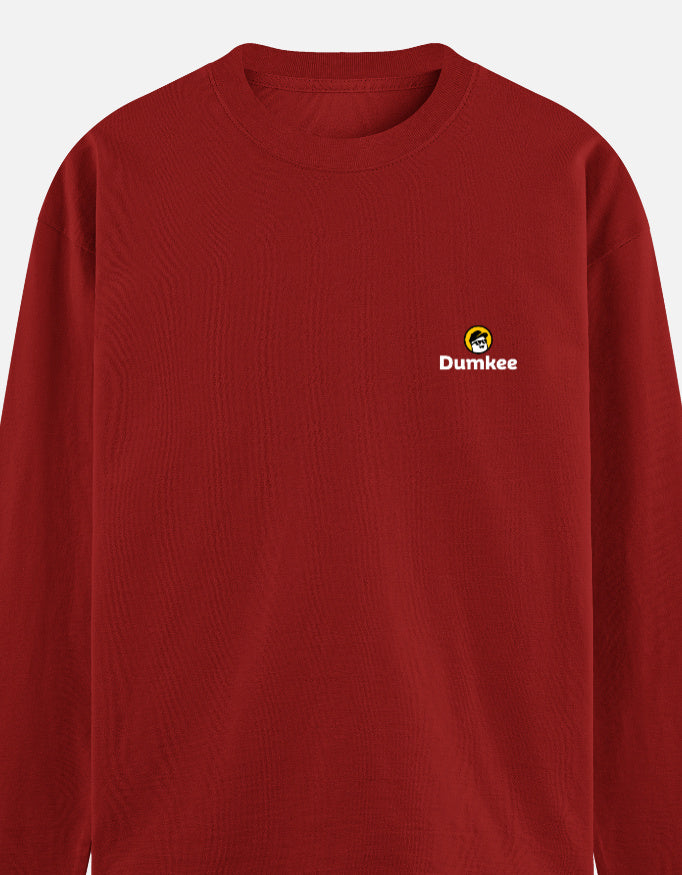 Man wearing a Dumkee red long-sleeve shirt with a logo standing in front of a door.