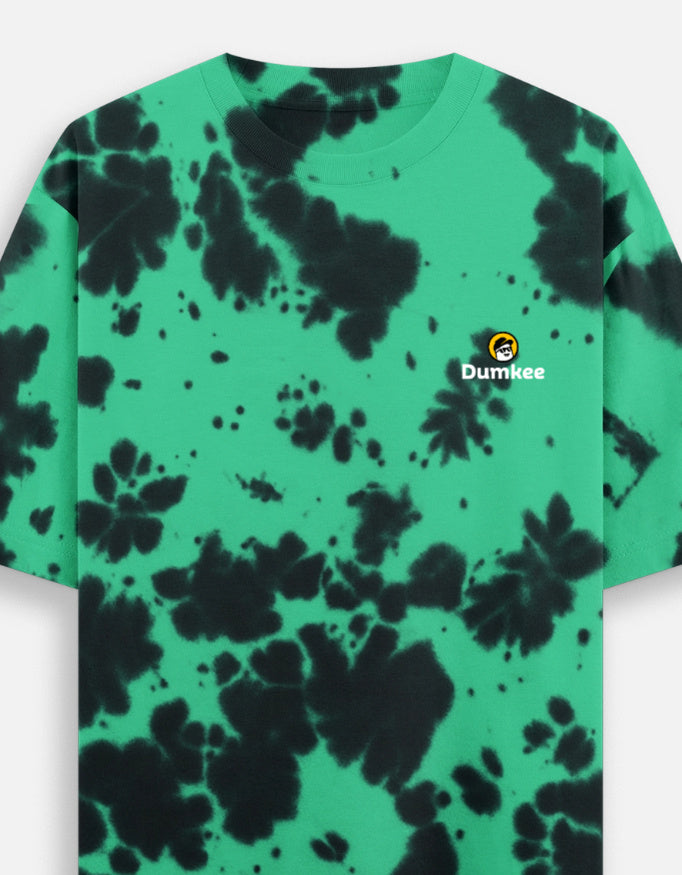 Person wearing a Dumkee Oversize green and black tie-dye t-shirt with a logo on a plain background