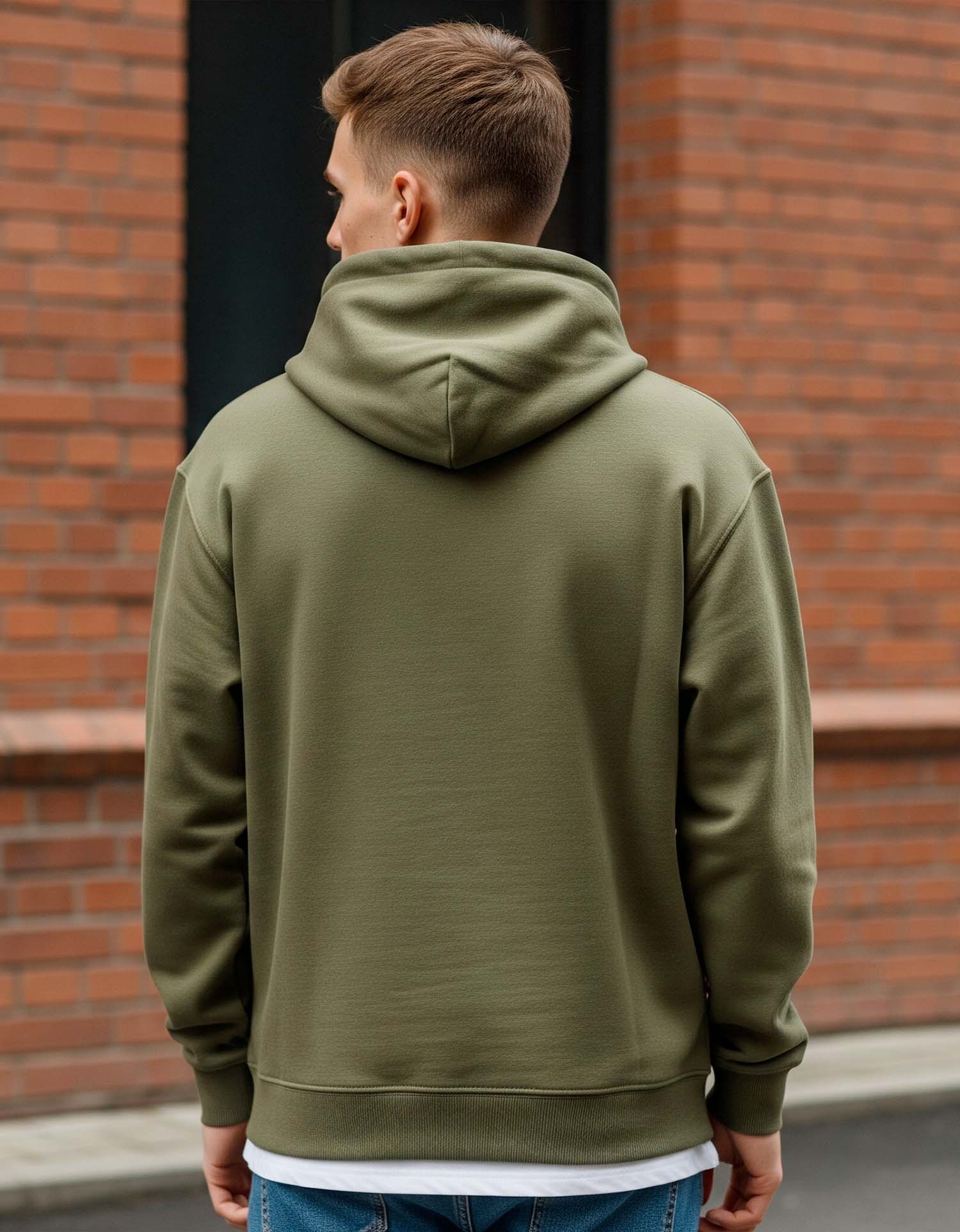 Man wearing a olive green hoodie standing against a brick wall.