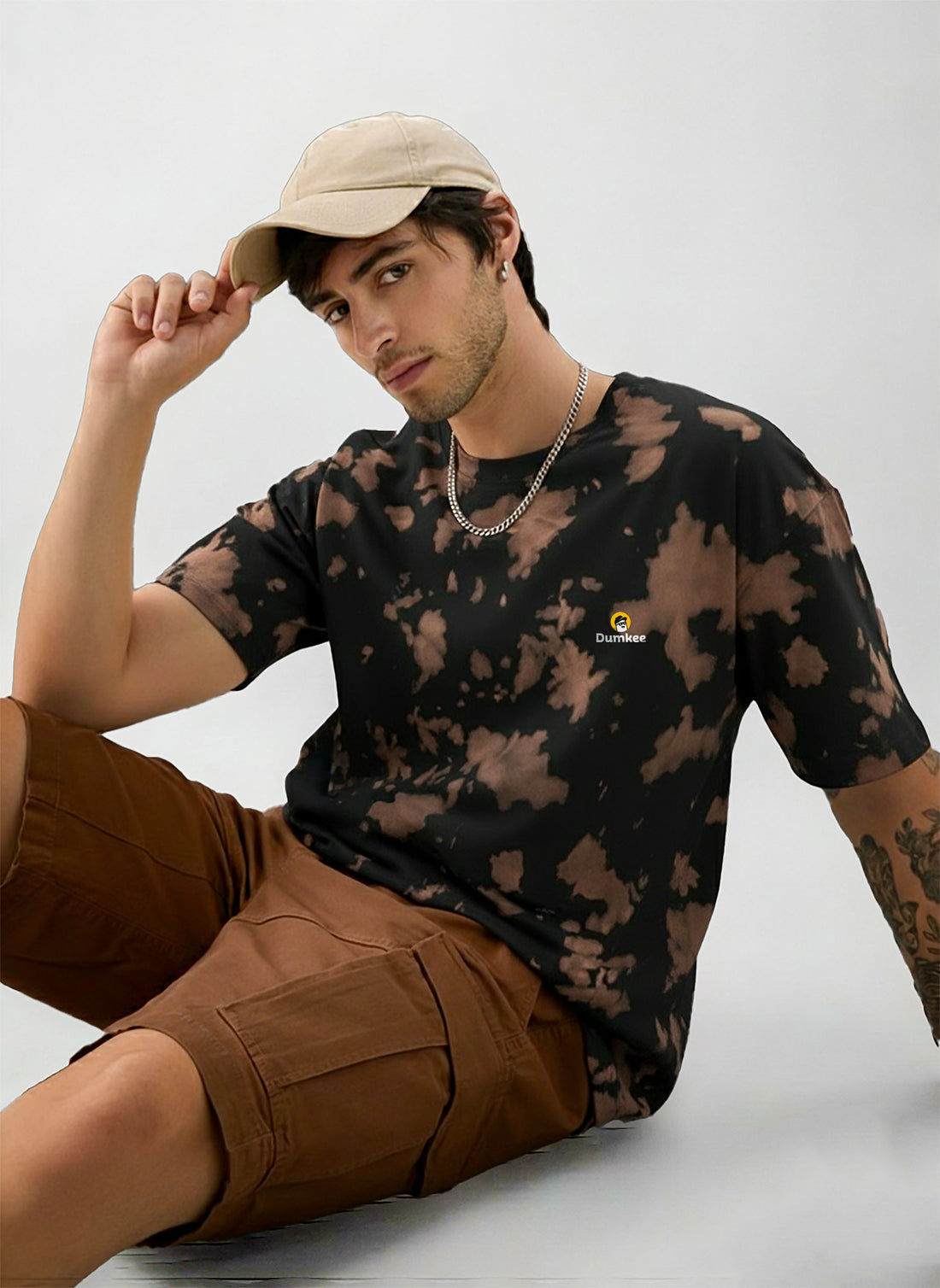 Man wearing a Dumkee Oversize black and brown tie-dye shirt with a beige cap