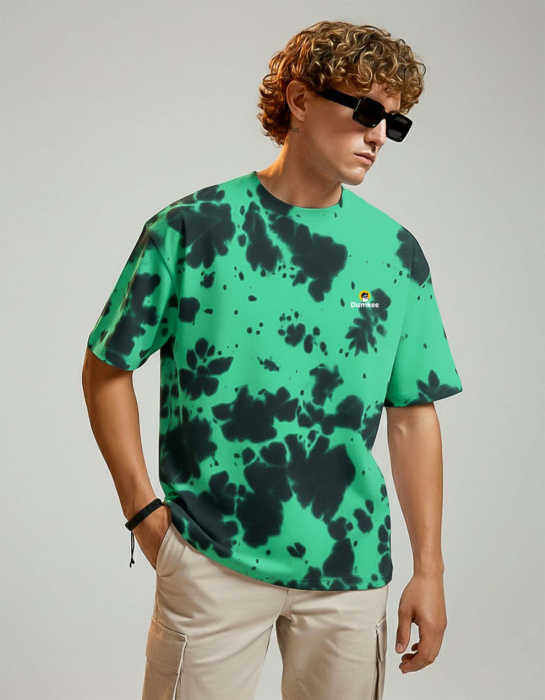 Person wearing a Dumkee Oversize green and black tie-dye t-shirt with a logo on a plain background