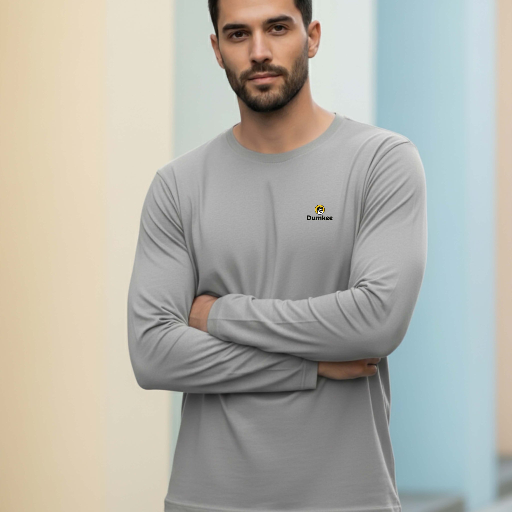 Man wearing a Dumkee gray long-sleeve shirt with a logo against a gradient background