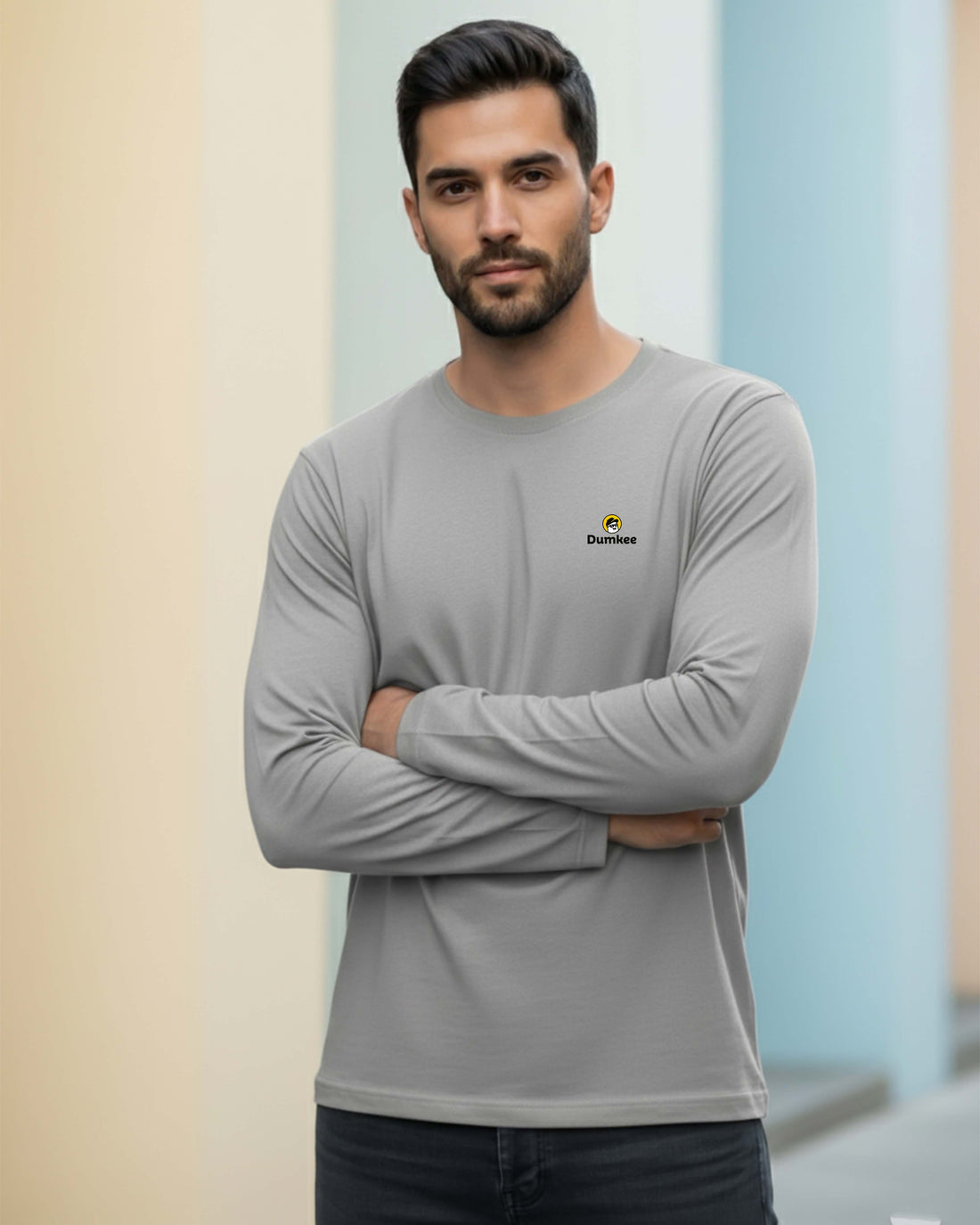 Man wearing a Dumkee gray long-sleeve shirt with a logo against a gradient background