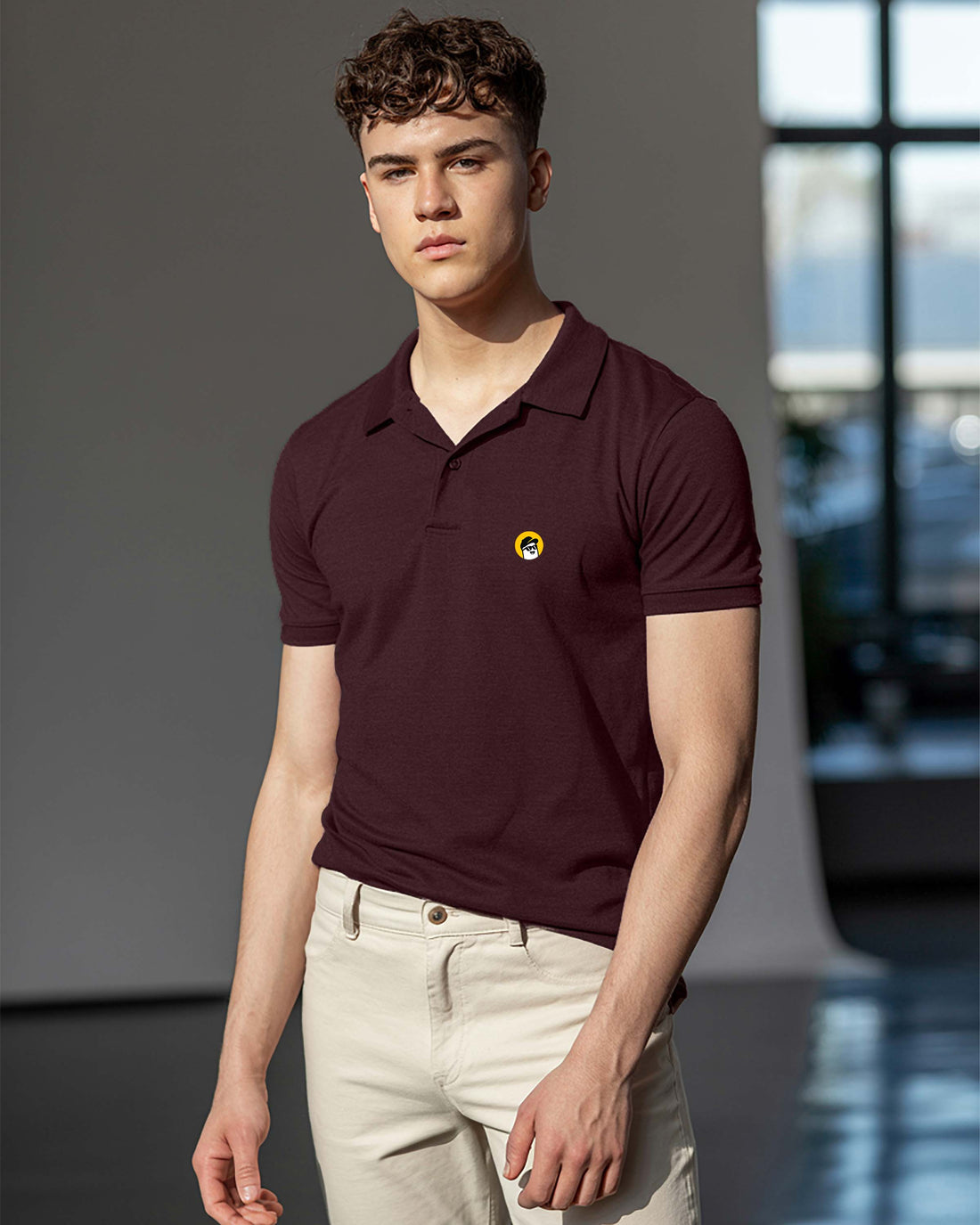 Man wearing a Dumkee maroon polo shirt with a yellow logo in an indoor setting