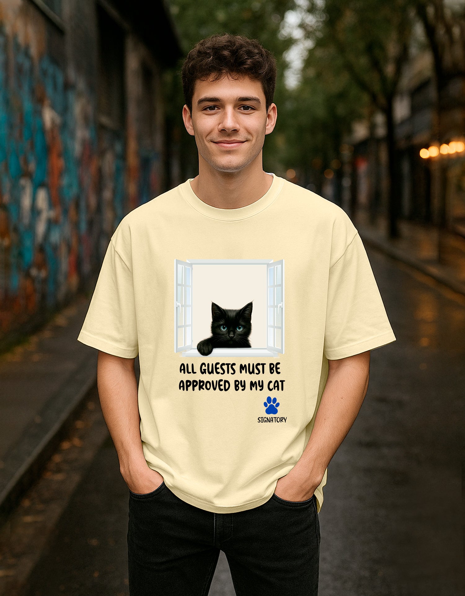 Person wearing a Dumkee beige oversize t-shirt with a cat graphic and text in an urban setting