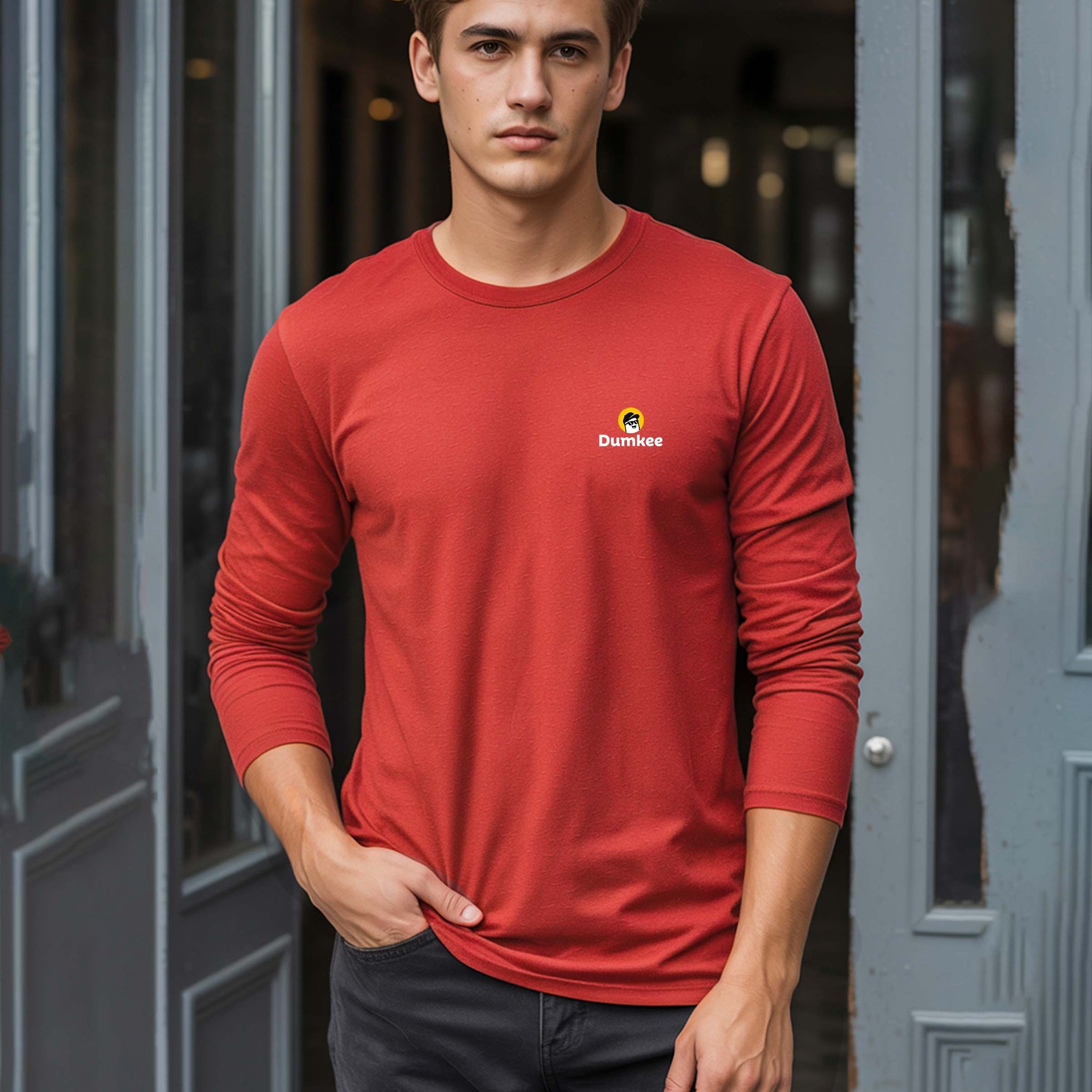 Man wearing a Dumkee red long-sleeve shirt with a logo standing in front of a door.