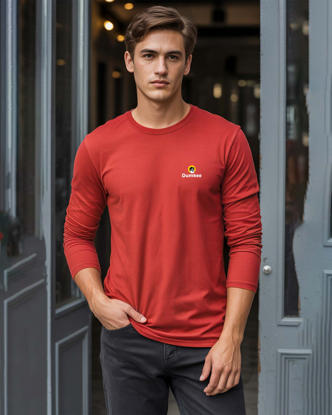 Man wearing a Dumkee red long-sleeve shirt with a logo standing in front of a door.