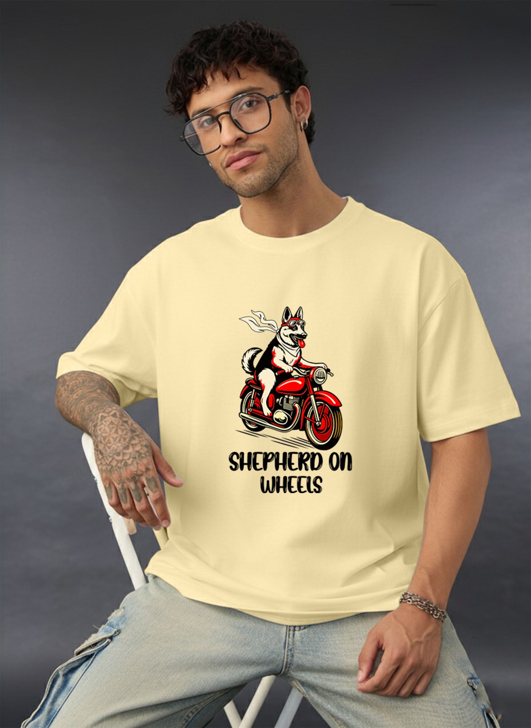Man wearing a Dumkee beige oversize t-shirt with a graphic of a shepherd on a motorcycle and text.