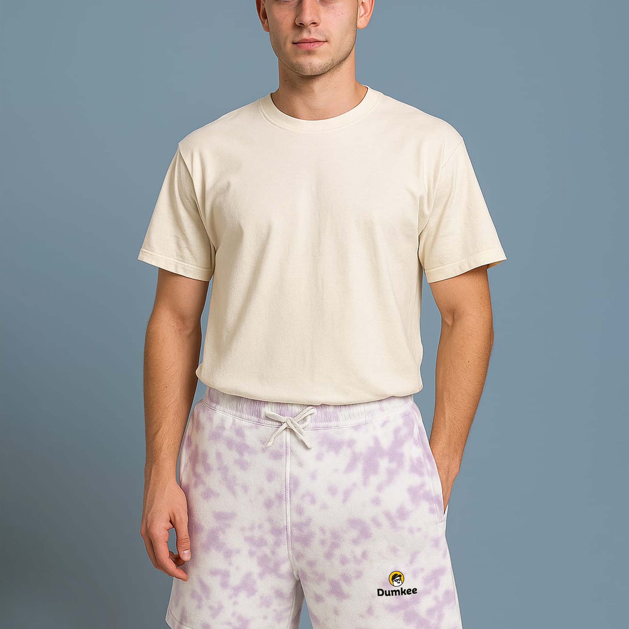 Man wearing a Dumkee beige t-shirt and purple tie-dye shorts with a brand logo