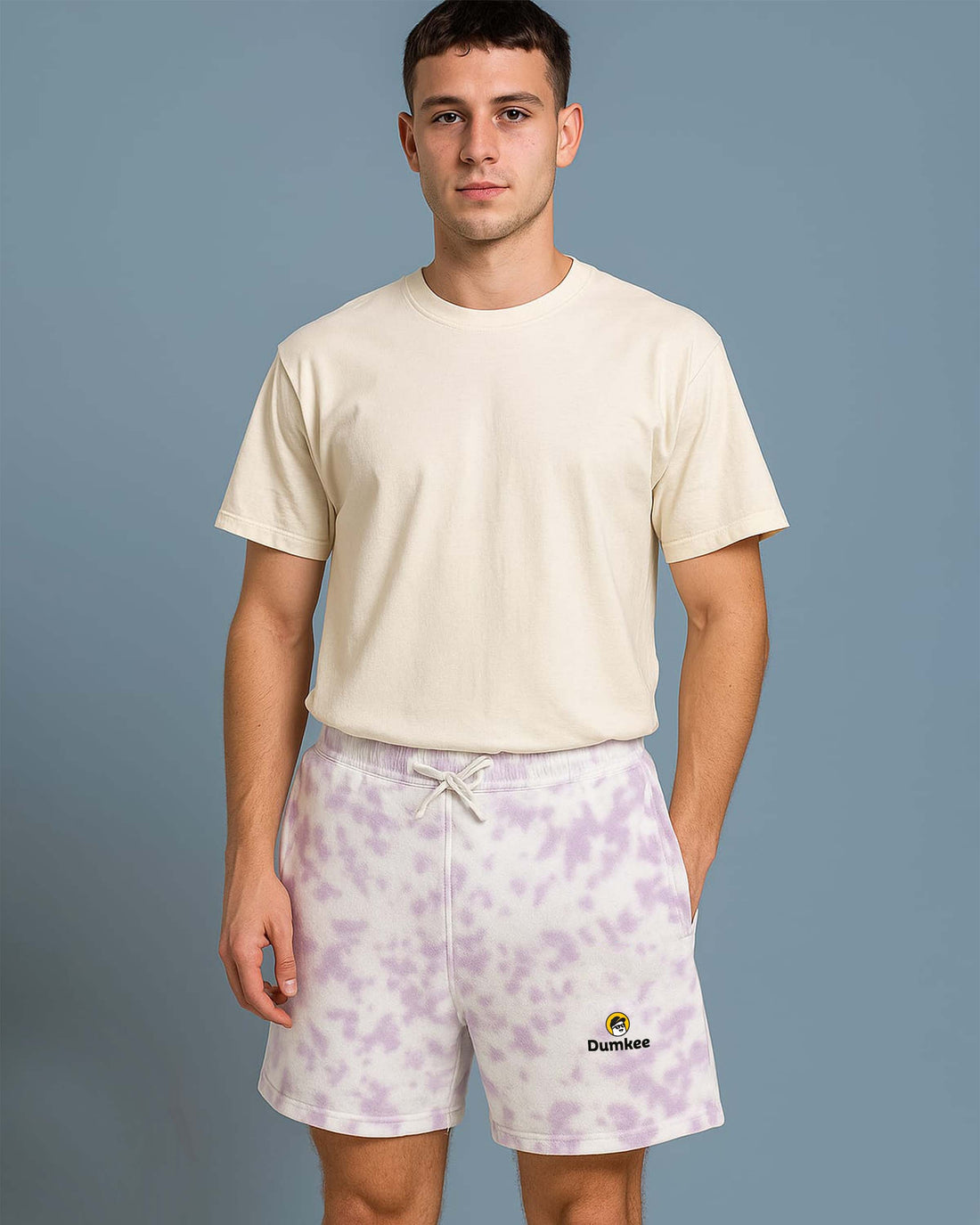 Man wearing a Dumkee beige t-shirt and purple tie-dye shorts with a brand logo